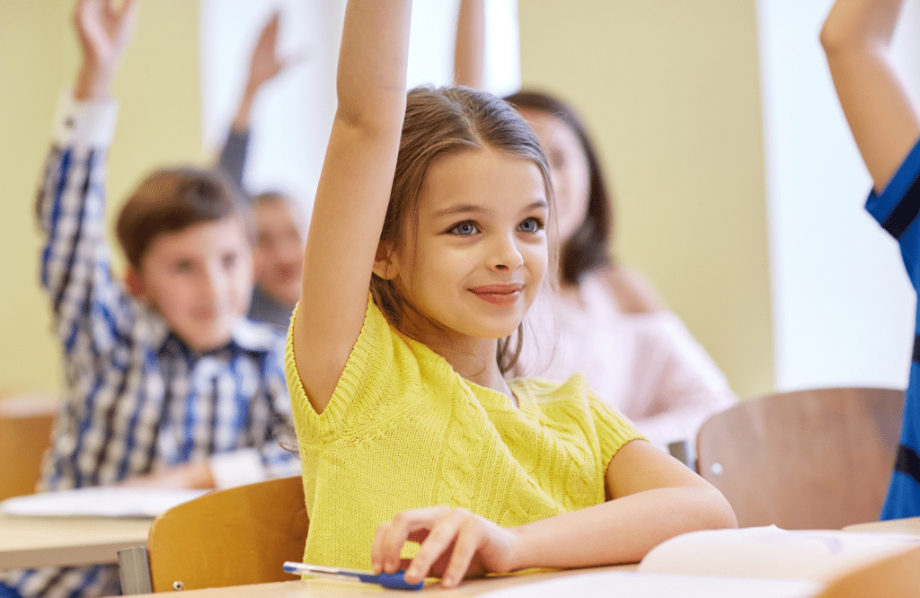 little girl in yellow sweater raising hand in class